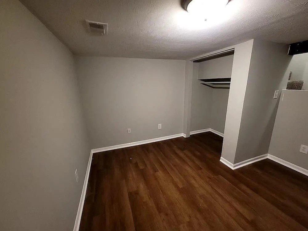 Finished basement bedroom with gray walls, dark plank flooring, and a closet